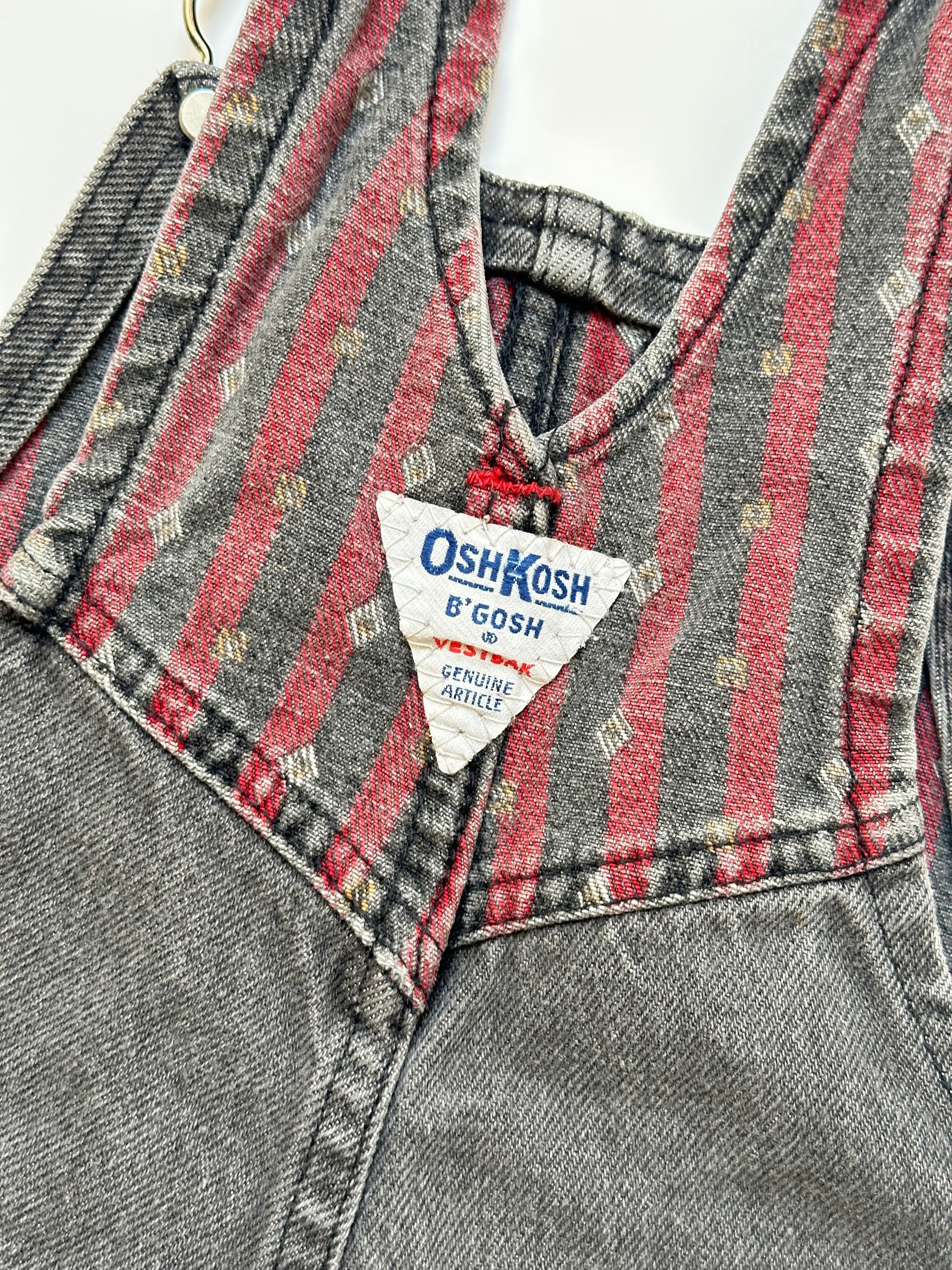 Kids vintage Grey and red denim dungarees with striped straps and Oshkosh brand label on a white background
