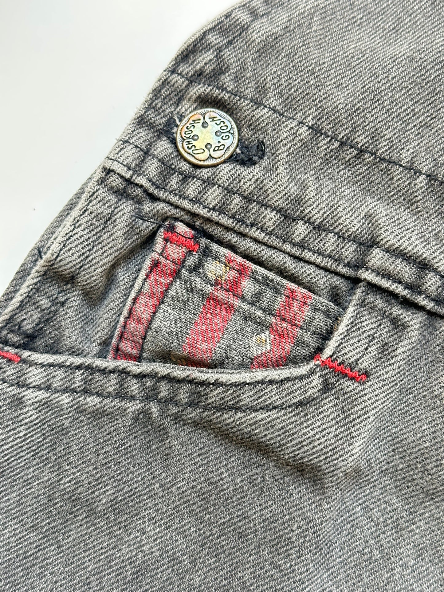 Kids vintage Grey and red denim dungarees with striped straps and Oshkosh brand label on a white background