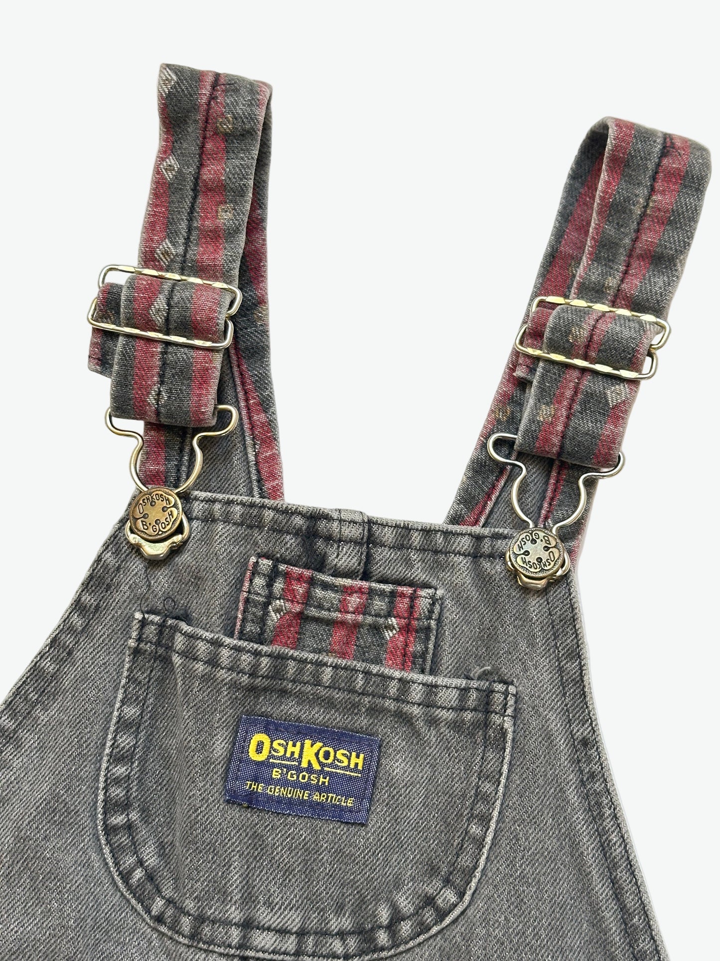 Kids vintage Grey and red denim dungarees with striped straps and Oshkosh brand label on a white background