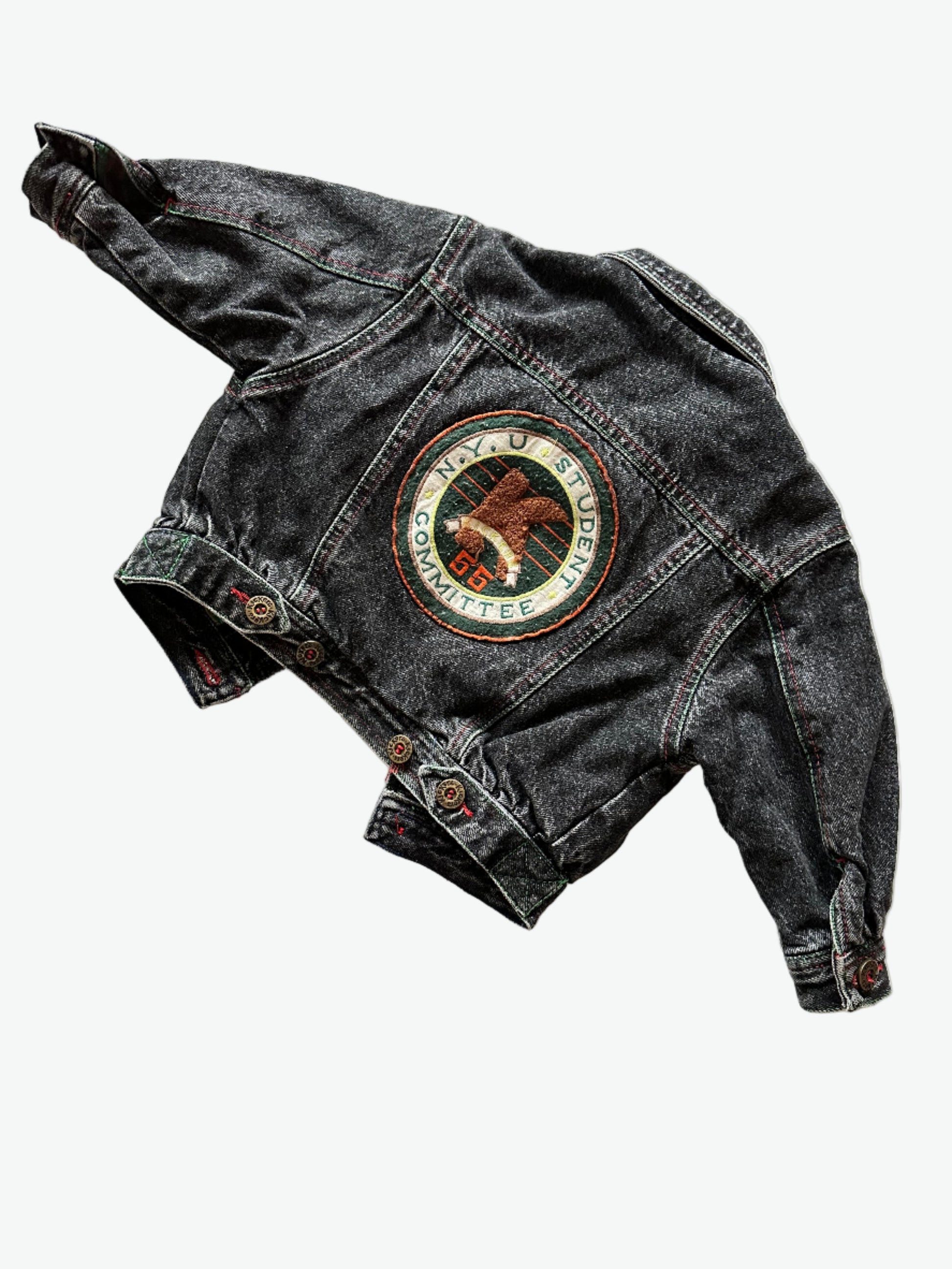 Kids vintage faded black Denim jacket with red stitching, brass buttons and a circular badge on the back on a white background