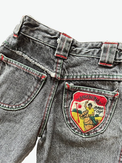 Close-up of Kids vintage faded black denim jeans with a colourful patch featuring a graphic design and text.