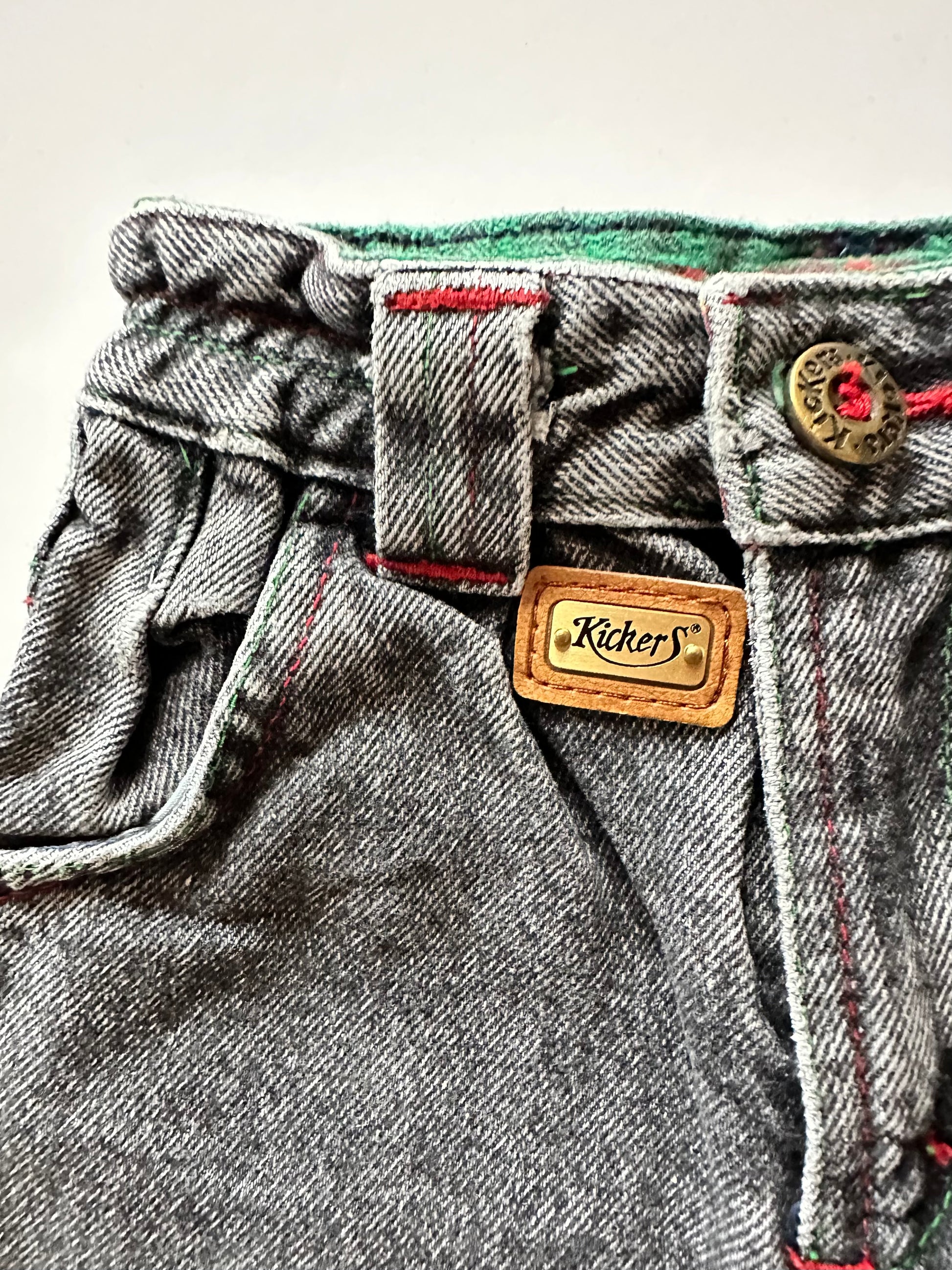 Kids vintage  faded black Denim jeans with red stitching highlights, brass buttons and unique badge details on a white background