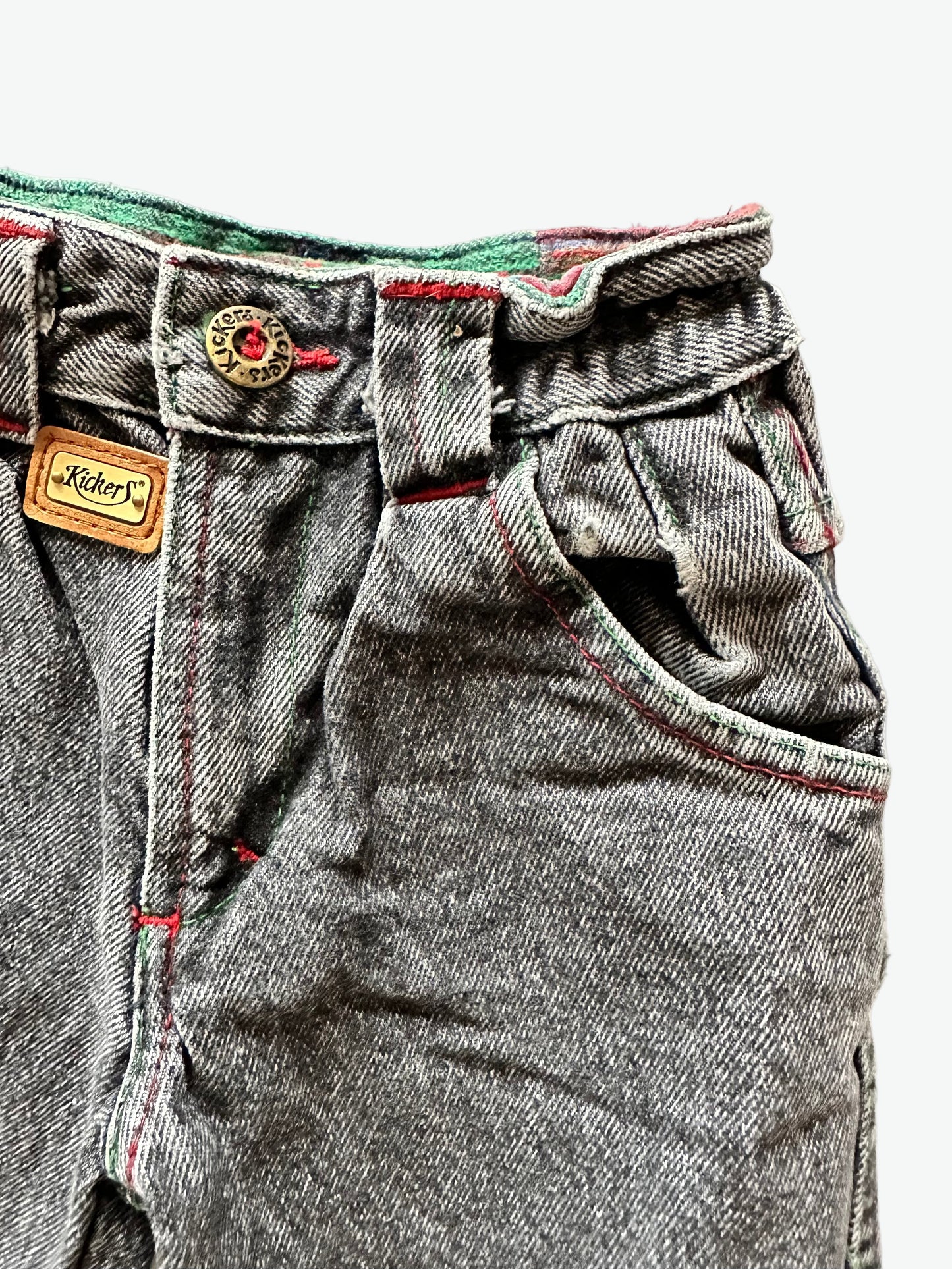 Close-up of a pair of kids vintage washed black jeans with a Kicker brand label on a white background