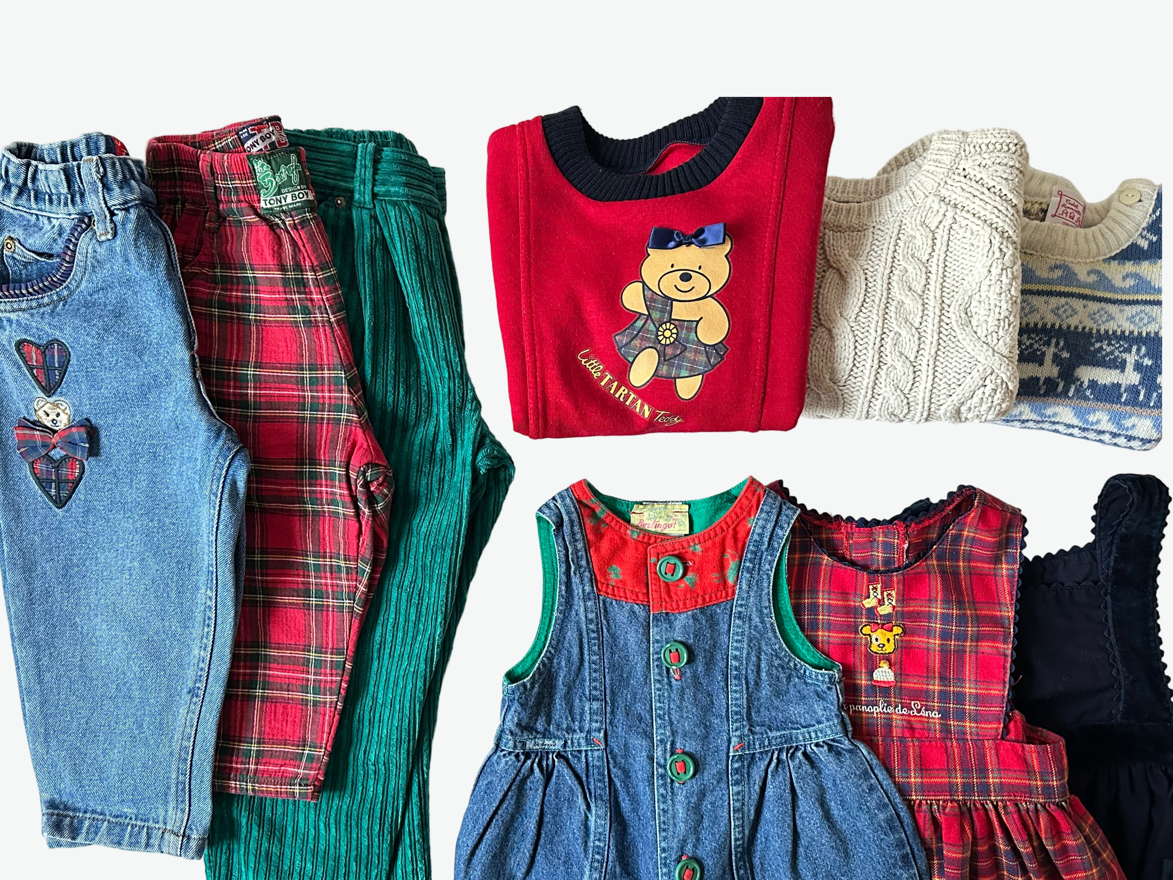 Kids vintage collection of children's clothing with Christmas in mind including jeans, check trousers, a red sweater dress with a bear design, and a denim romper on a white surface.