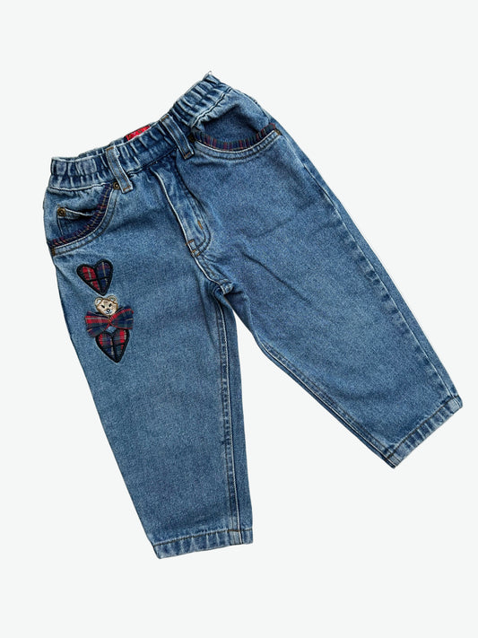 Pair of blue jeans with check heart patches, a bow and a bear on the thigh, check frills around the pockets on a white background