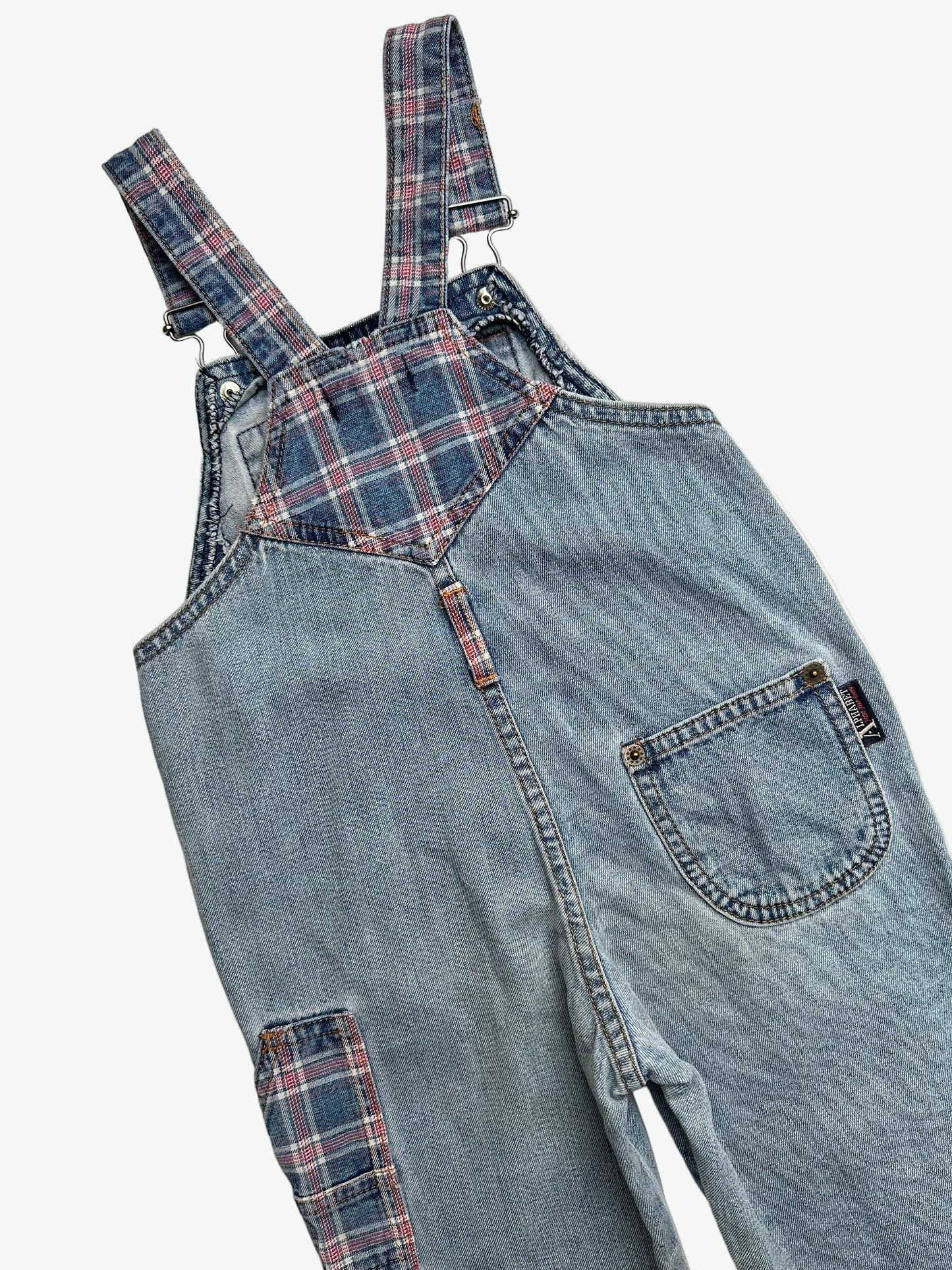 Kids vintage blue denim dungarees with check details and badge on chest pocket laid flat on a white background.