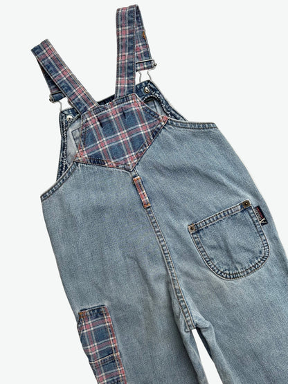 Kids vintage blue denim dungarees with check details and badge on chest pocket laid flat on a white background.