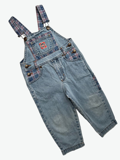 Kids vintage blue denim dungarees with check details and badge on chest pocket laid flat on a white background.