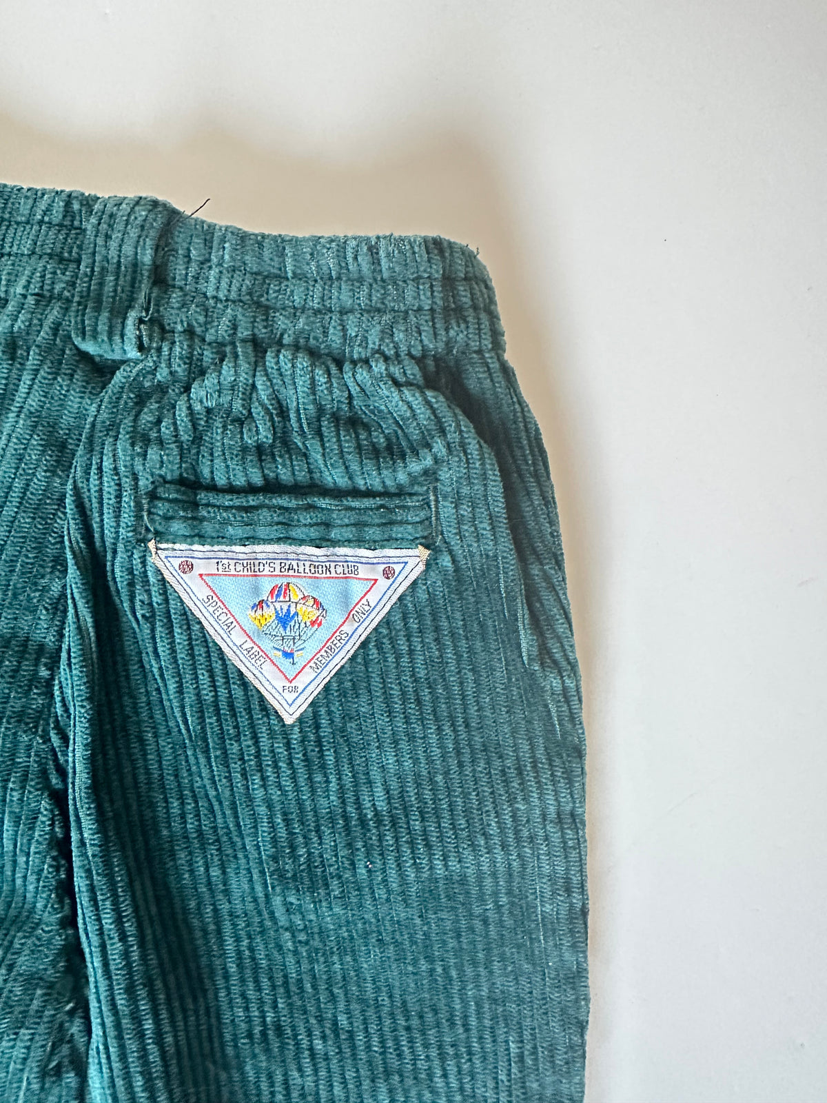 Dark green corduroy pants with a triangle label on a light background