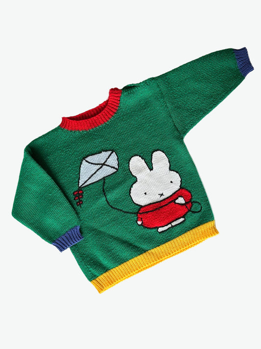 Green hand knit jumper with blue yellow and red details and with miffy/nijntje character and kite design on a white background.