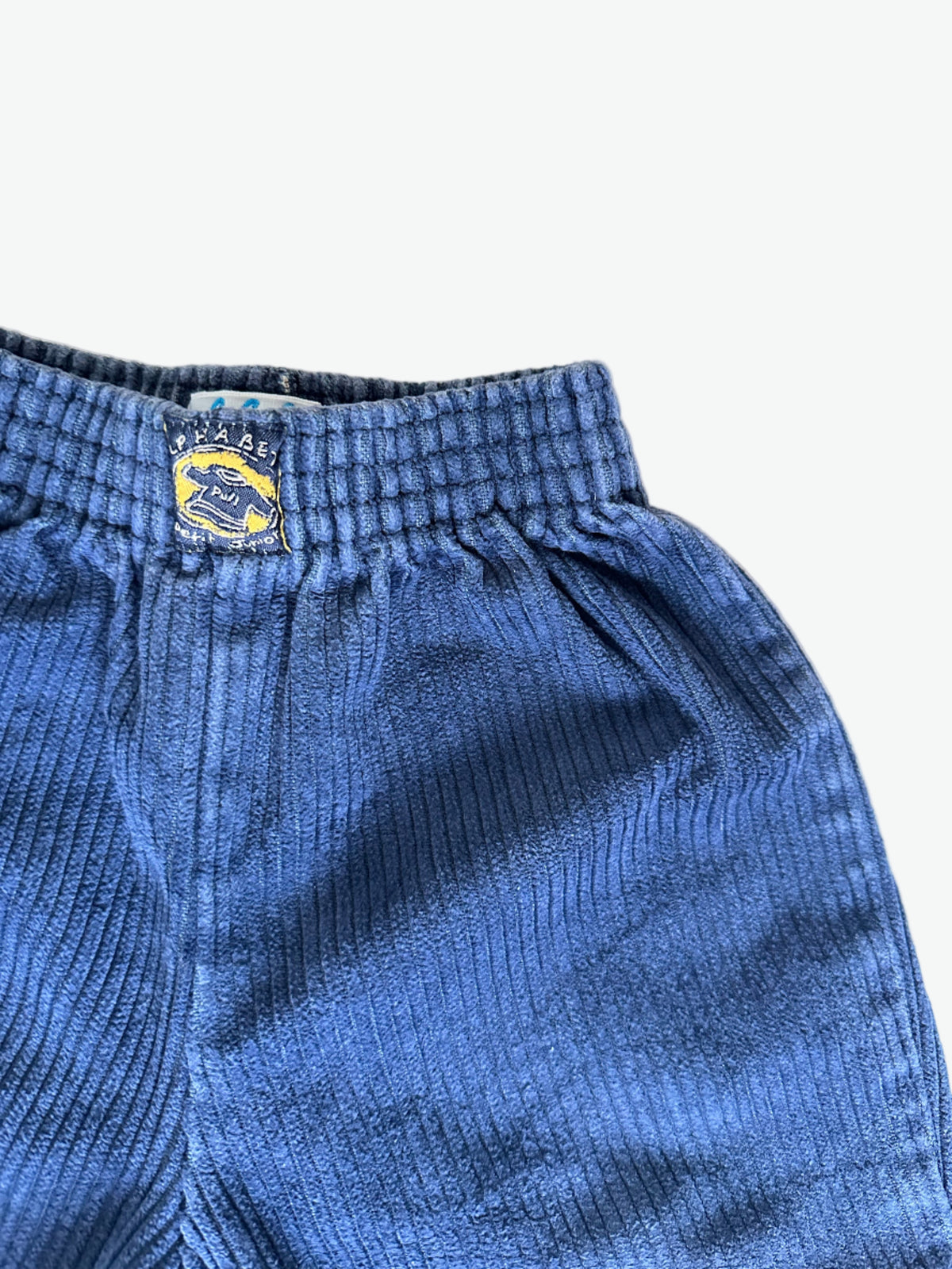 Close-up of inky blue corduroy pants with a brand logo on a white background