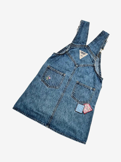 Kids vintage OshKosh dungaree dress, featuring ditsy floral lining inside the top, delicate embroidered flowers, and playful patch details. Mid-wash denim with classic OshKosh branding, it’s finished with antique brass trimmings and sturdy dungaree buckles. Age 4 years.