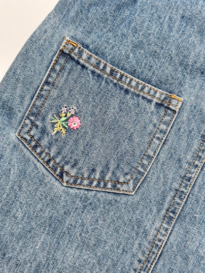 Kids vintage OshKosh dungaree dress, featuring ditsy floral lining inside the top, delicate embroidered flowers, and playful patch details. Mid-wash denim with classic OshKosh branding, it’s finished with antique brass trimmings and sturdy dungaree buckles. Age 4 years.