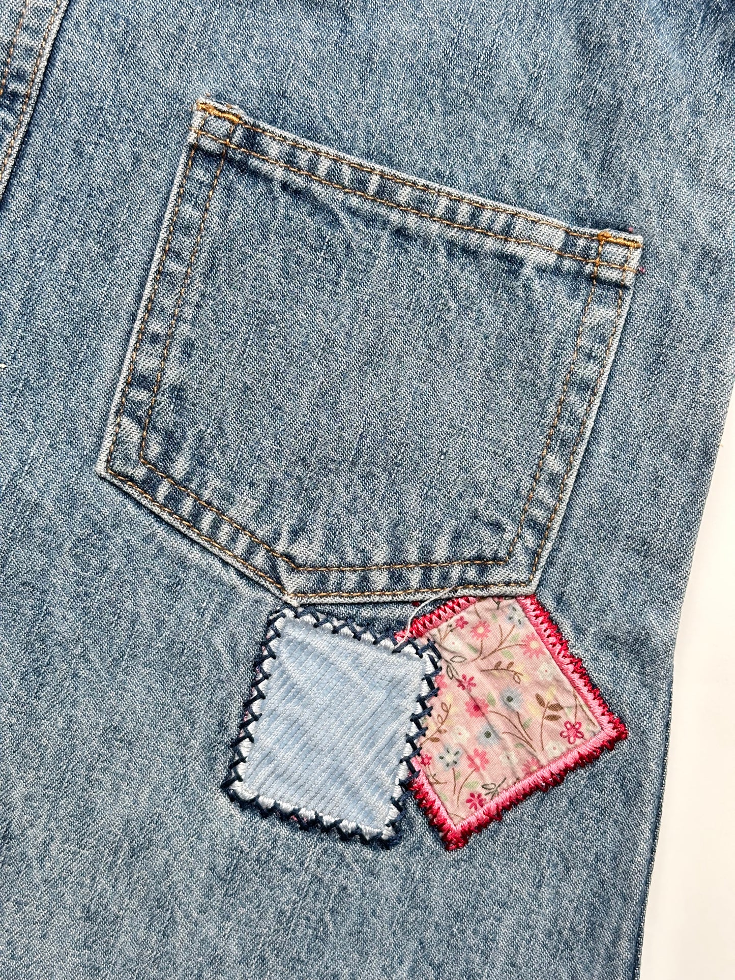 Kids vintage OshKosh dungaree dress, featuring ditsy floral lining inside the top, delicate embroidered flowers, and playful patch details. Mid-wash denim with classic OshKosh branding, it’s finished with antique brass trimmings and sturdy dungaree buckles. Age 4 years.