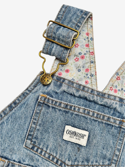 Kids vintage OshKosh dungaree dress, featuring ditsy floral lining inside the top, delicate embroidered flowers, and playful patch details. Mid-wash denim with classic OshKosh branding, it’s finished with antique brass trimmings and sturdy dungaree buckles. Age 4 years.