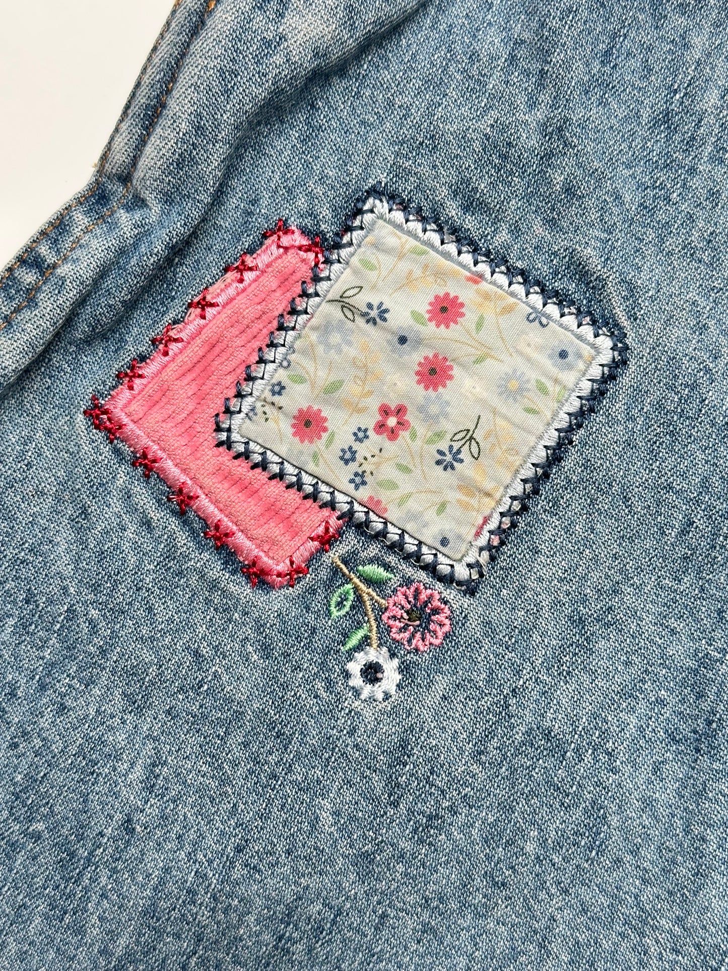 Kids vintage OshKosh dungaree dress, featuring ditsy floral lining inside the top, delicate embroidered flowers, and playful patch details. Mid-wash denim with classic OshKosh branding, it’s finished with antique brass trimmings and sturdy dungaree buckles. Age 4 years.