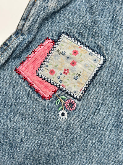 Kids vintage OshKosh dungaree dress, featuring ditsy floral lining inside the top, delicate embroidered flowers, and playful patch details. Mid-wash denim with classic OshKosh branding, it’s finished with antique brass trimmings and sturdy dungaree buckles. Age 4 years.