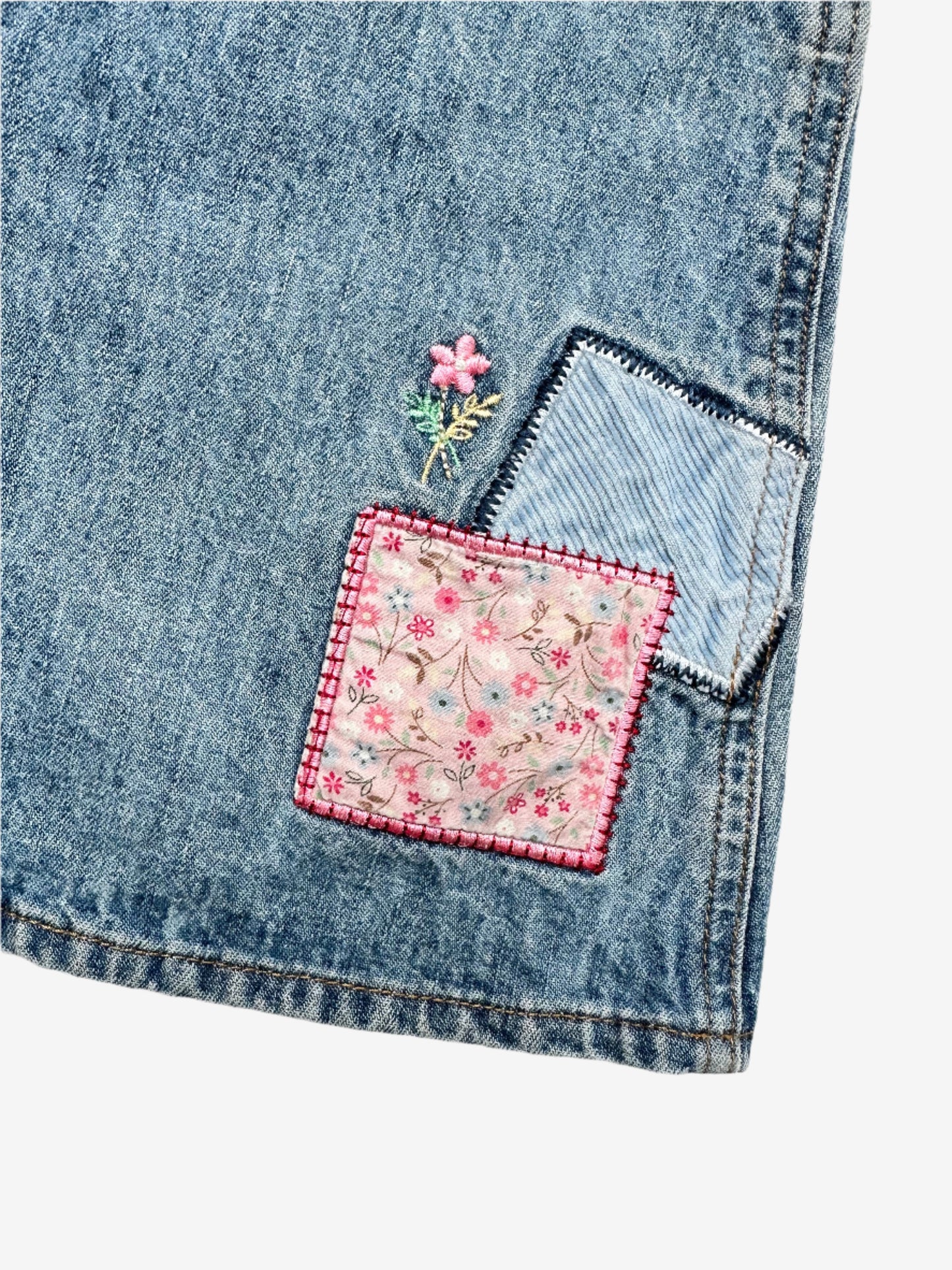 Kids vintage OshKosh dungaree dress, featuring ditsy floral lining inside the top, delicate embroidered flowers, and playful patch details. Mid-wash denim with classic OshKosh branding, it’s finished with antique brass trimmings and sturdy dungaree buckles. Age 4 years.