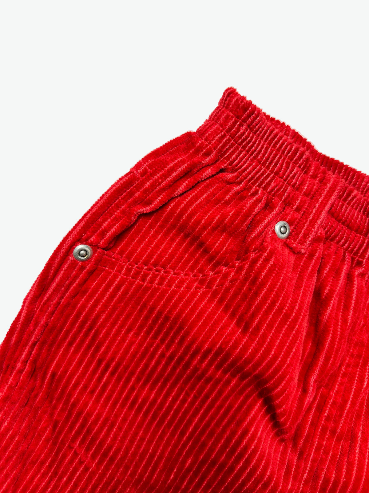 Close-up of red corduroy trousers with rivets on a white background