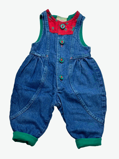 True blue denim romper with red patches that has a festive print, green buttons and lined with green on a white background